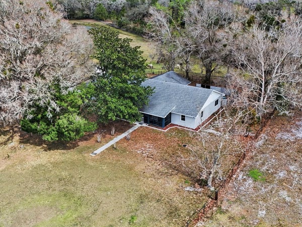 Aerial photo of the house with a front sidewalk as well as a rear entry sidewalk located off of the two car garage and paved slab parking area. This home is surrounded by mature trees and landscaping!