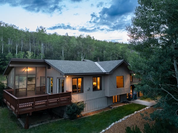 This spacious home features large windows and outdoor space, set against a lush, wooded backdrop.