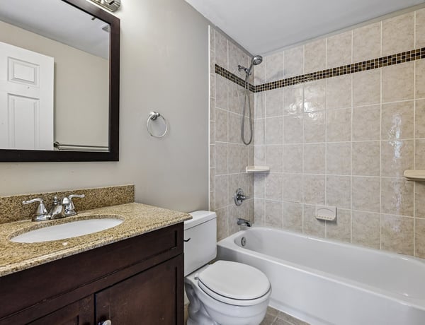 Modern bathroom featuring granite countertops, clean tilework, and a convenient shower-tub combination.