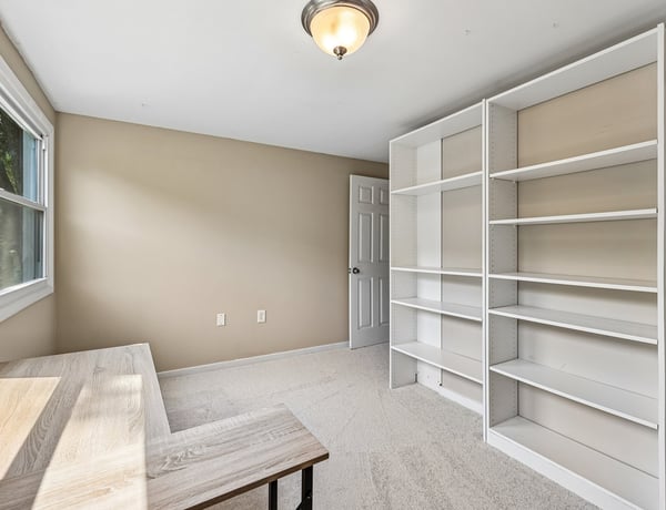 Bright and spacious room featuring built-in shelving and large windows, perfect for a home office or study.