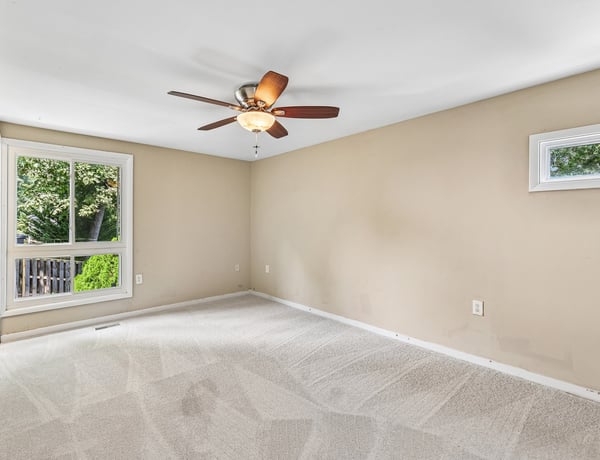 Bright and spacious room featuring new carpet, a ceiling fan, and a view of the outdoors.