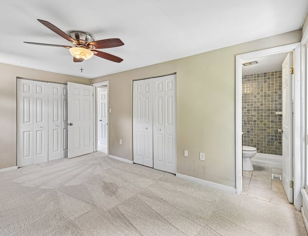Spacious bedroom featuring a ceiling fan, multiple closets, and an adjoining bathroom for convenient living.