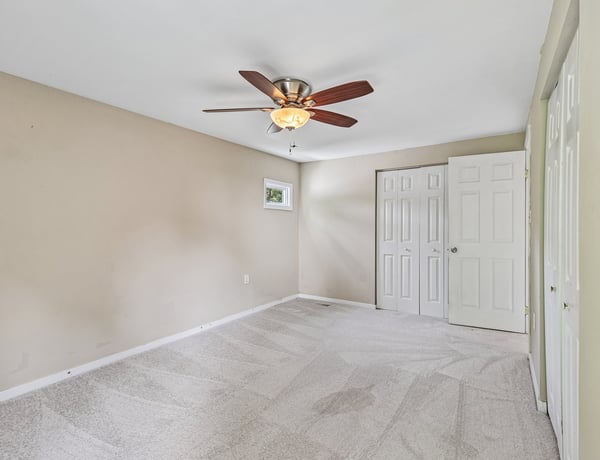 Spacious bedroom featuring a ceiling fan, large windows, and ample storage with double closets.