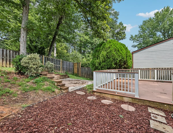 This inviting backyard features a spacious deck, lush greenery, and a stone pathway for easy access.